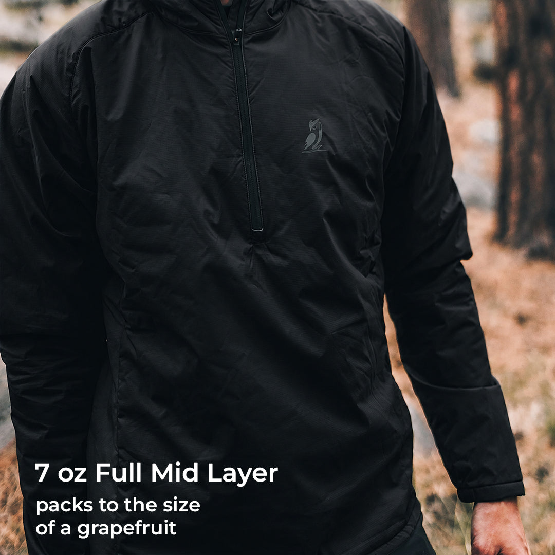 A person wearing a black lightweight zip-front mid layer jacket outdoors, with text overlay at the bottom reading '7 oz Full Mid Layer packs to the size of a grapefruit'.