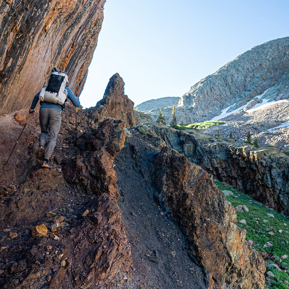 rear view of man wearing ultralight backpack for thru-hiking while climbing steep incline