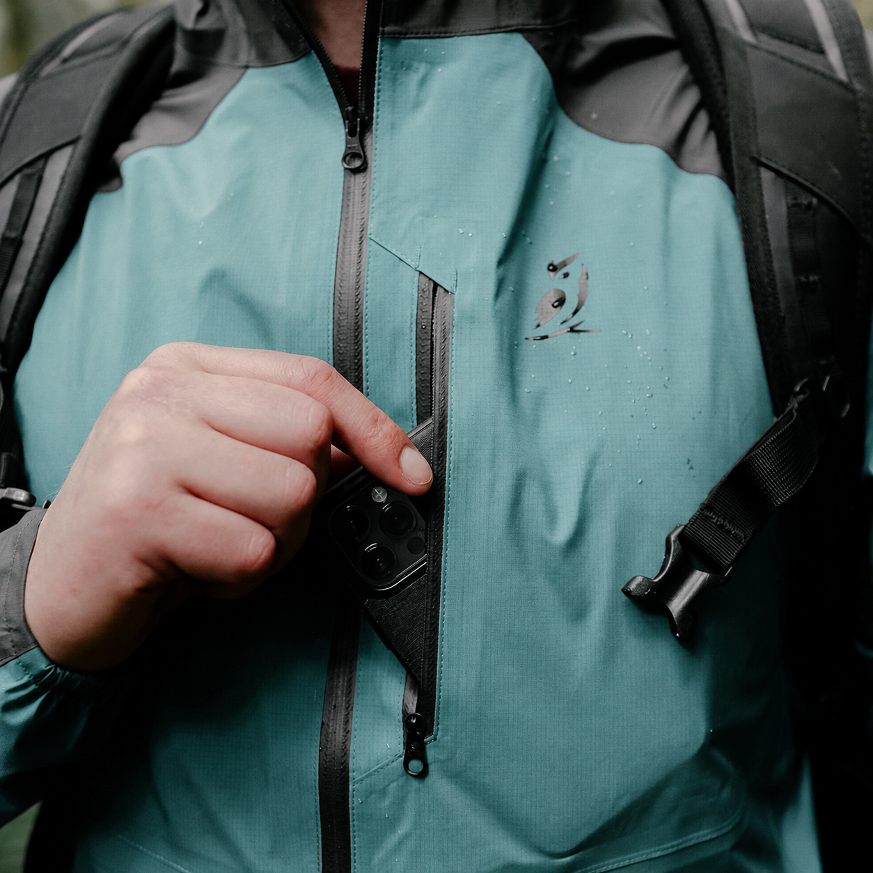 Close-up of a person wearing a waterproof jacket with a black backpack, opening a zippered pocket on the chest.