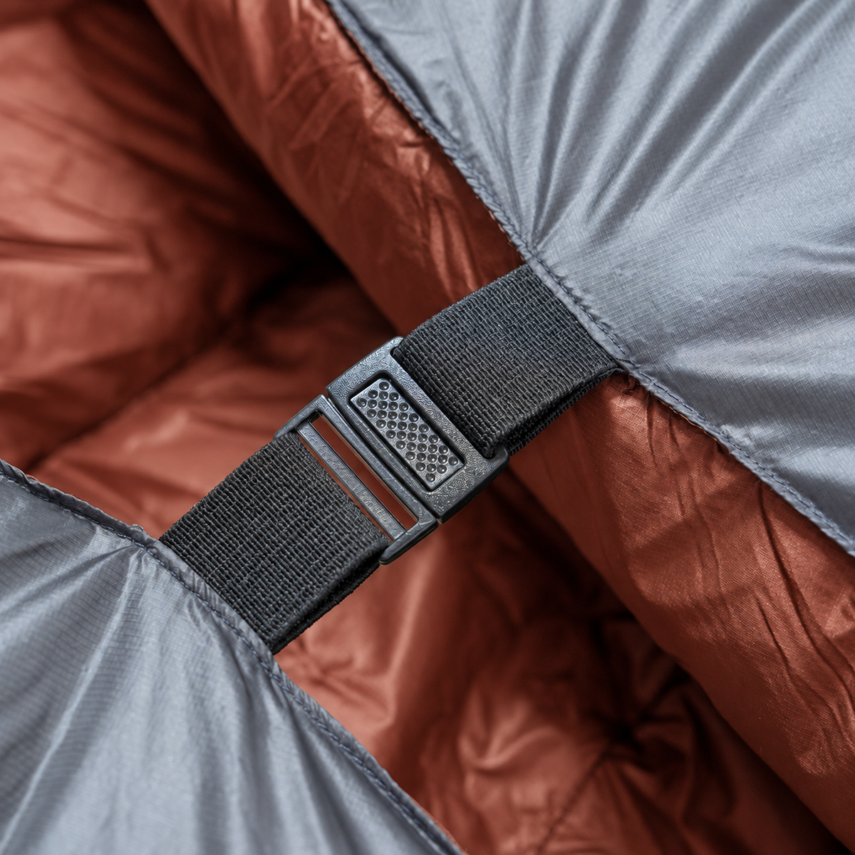 Close-up of a buckle and strap securing two sides of a backpacking quilt with a red interior together.