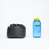 Compressed gray backpacking quilt in its stuff sack shown next to a blue Nalgene water bottle for size comparison.