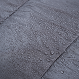 Close-up of water droplets beading on the surface of a gray quilt fabric, showing its water-resistant properties.