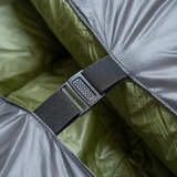 Close-up of a black buckle and strap securing two sides of a gray and green backpacking quilt together.
