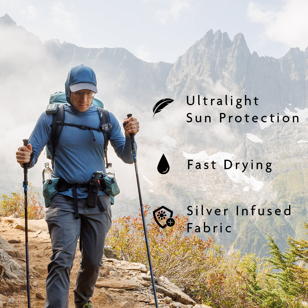 Blue - A hiker wearing a long-sleeve performance shirt on a mountain trail with misty peaks in the background.