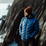 front view of man wearing blue down jacket & keeping hands warm in insulated pockets
