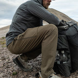 close side view of man crouching on mountain peak showing the flexibility of his hiking pants