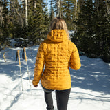 Woman wearing insulated hooded down jacket from the back while walking through snowy forest terrain.