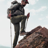 side view of man taking large step onto stony peak while wearing backpacking gear & clothing