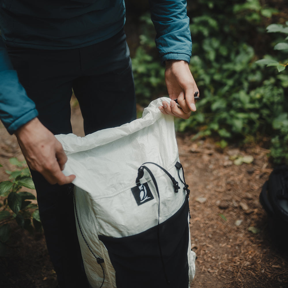 front view of man closing roll-top of ultralight backpack on the trail