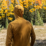 Person wearing a golden hooded sun shirt standing in a forest with autumn foliage.