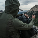 rear view of man wearing green fleece hoodie on top of rugged mountain peak