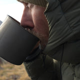 Camper sipping from a titanium mug while bundled in the Outdoor Vitals Vantage jacket, showcasing warmth and comfort for cold-weather backpacking.