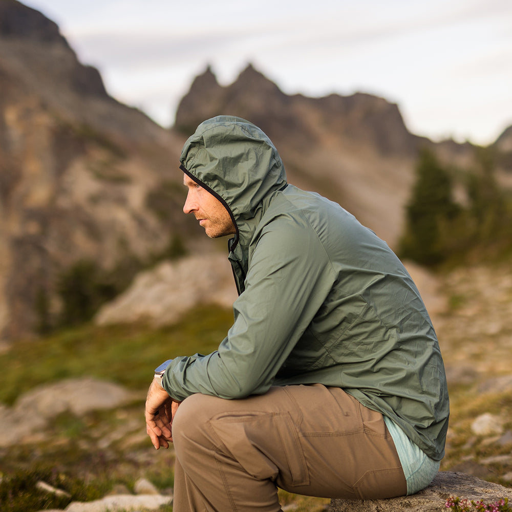 Side view of hiker wearing Nebo Windbreaker with hood up, Nebo Windbreaker side profile, Man sitting outdoors in Nebo Windbreaker jacket
