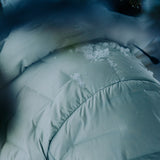 Close-up of a light gray Outdoor Vitals insulated jacket with snow resting on the shoulder and hood, showing the fabric’s weather resistance.