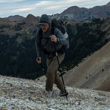 side view of man hiking up steep mountain with a backpack on