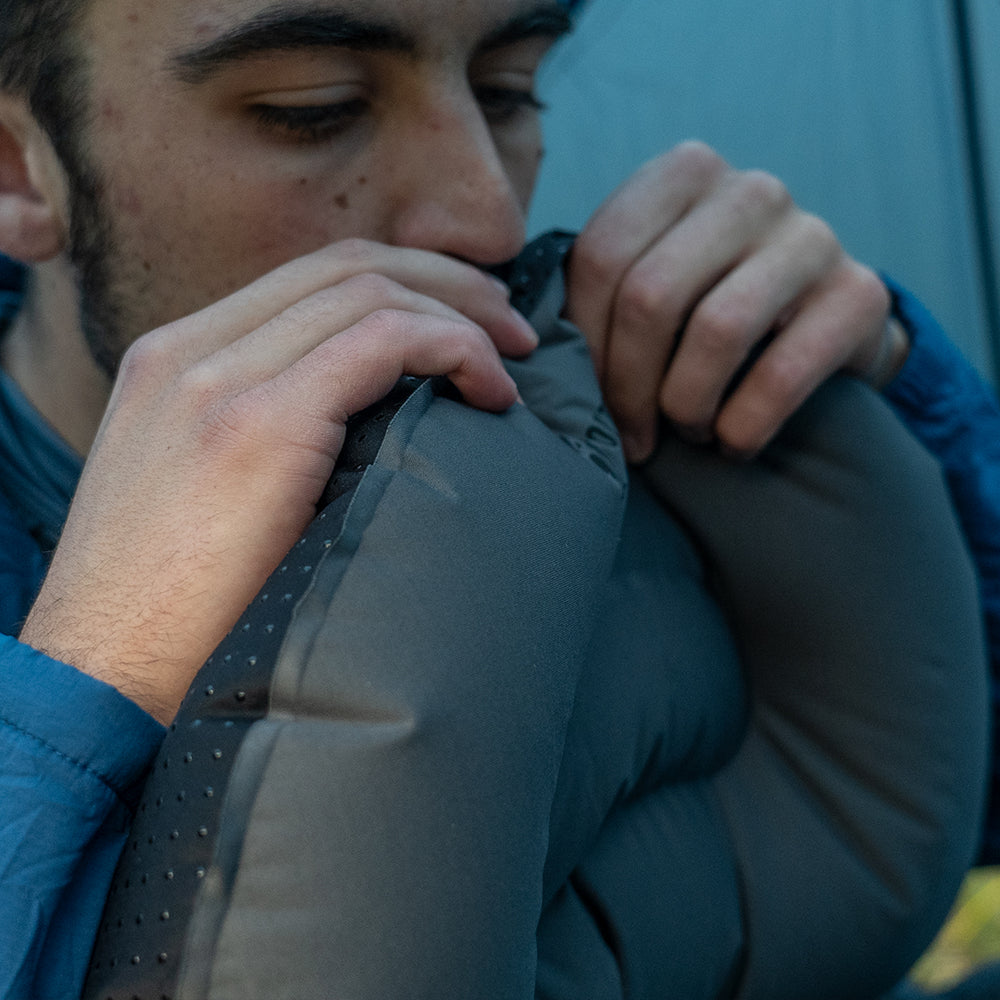 close view of man inflating ultralight pillow inside of backpacking tent