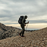 side view of man hiking on rocky mountain ridge while wearing backpacking gear