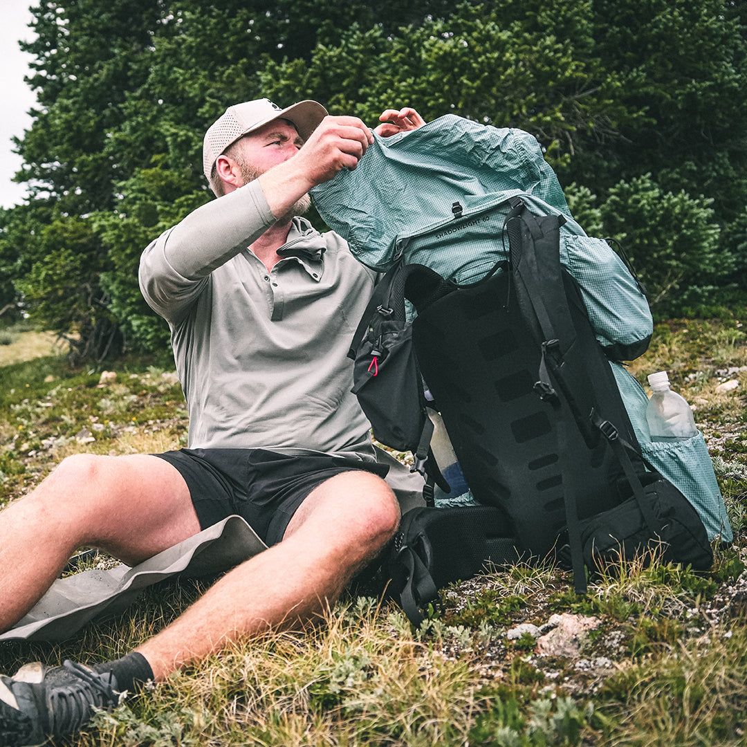 hiker removes gear from backpack while sitting on the ground near a tree
