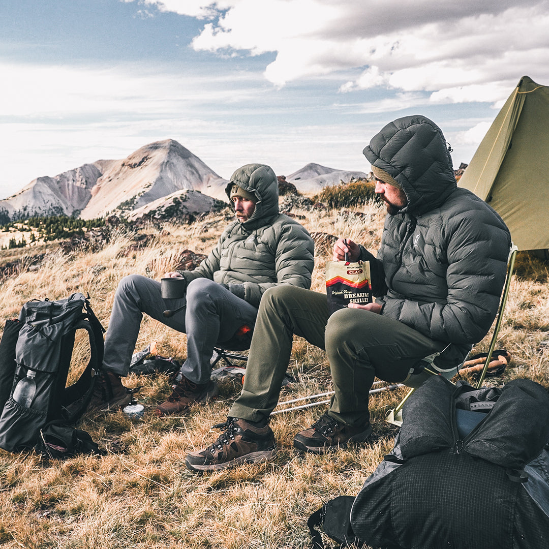2 backpackers sitting at high elevation camp while wearing puffy down jackets