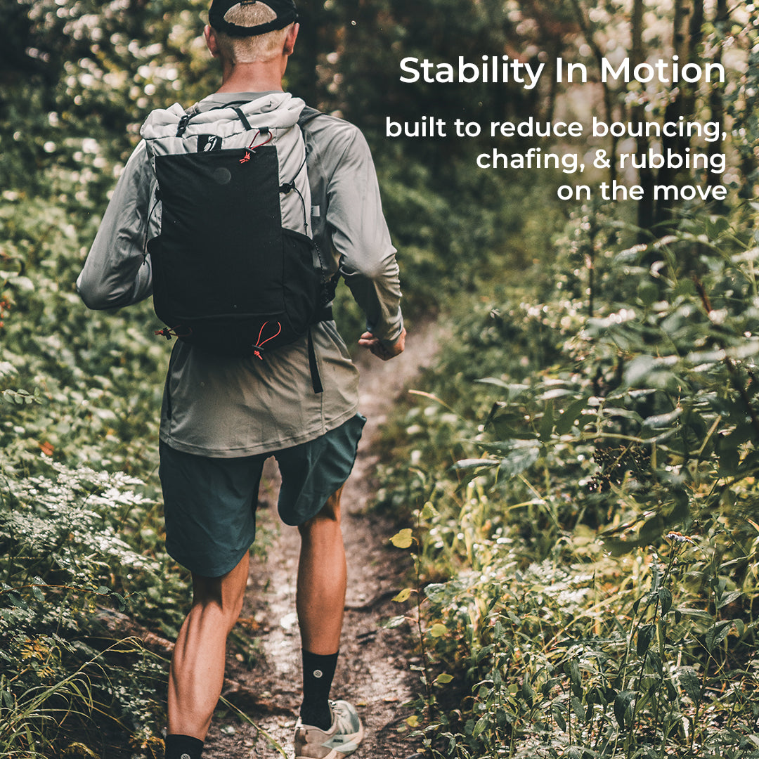 rear view of fastpacker running down narrow trail in a wooded area. Text callout says, "Stability In Motion - built to reduce bouncing, chafing, & rubbing on the move."