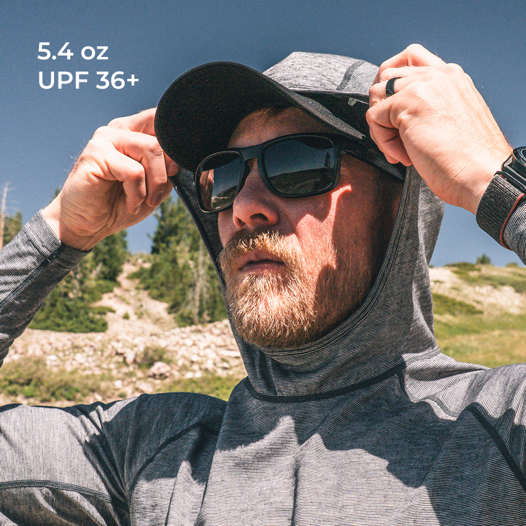 A man outdoors wearing a high-neck sun protection hooded shirt, baseball cap, and sunglasses.