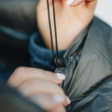 Close-up of a person tightening the drawstring and cord lock on a gray insulated sleeping bag, adjusting the fit for warmth.