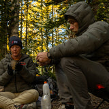 Backpackers wearing Outdoor Vitals Vantage Alpine Down Jackets while preparing a warm meal at a forest campsite in cool weather.