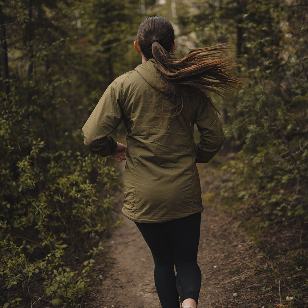 rear view of woman trail running through forest wearing green performance hoodie