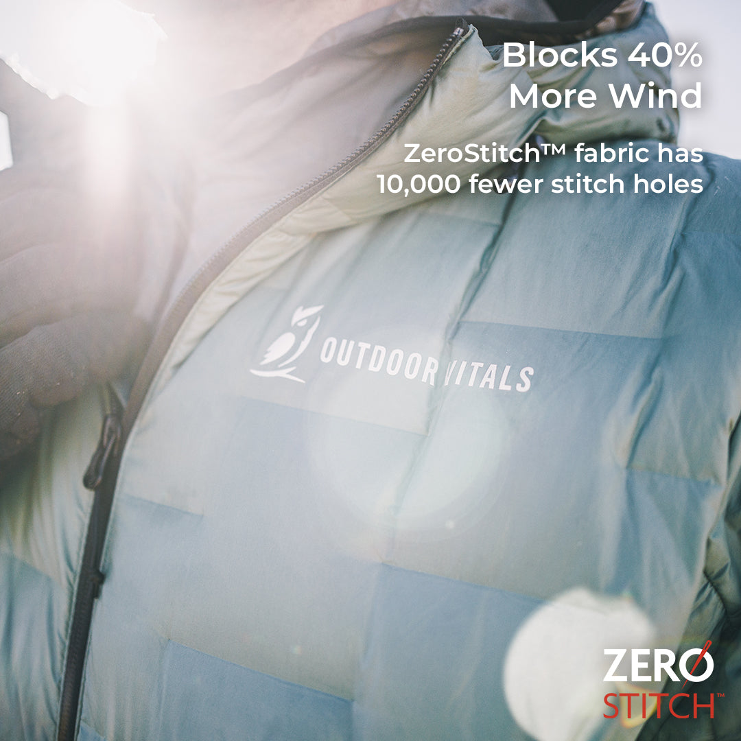 A close-up of a person wearing a puffer jacket in bright sunlight. The jacket is light blue with a visible 'OUTDOOR VITALS' logo on the chest and promotional text overlaid about ZeroStitch fabric.