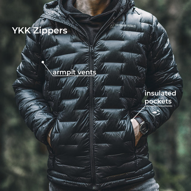 A person wearing a black quilted puffer jacket in a dark outdoor setting, with white text callouts pointing to YKK zippers, armpit vents, and insulated pockets.