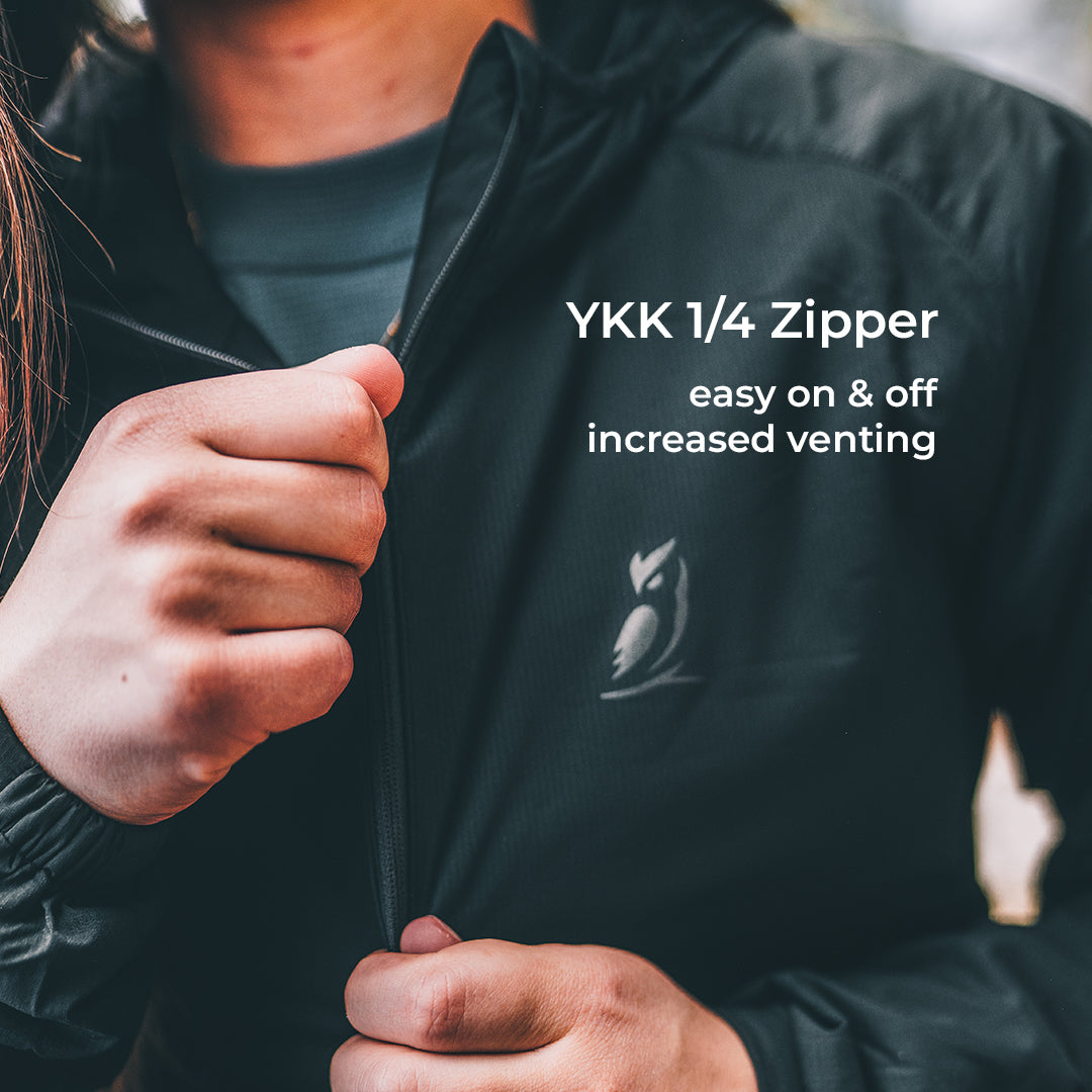Close-up of a person wearing a black lightweight jacket and unzipping the collar with a 1/4 zipper. White text on the right reads 'YKK 1/4 Zipper easy on & off increased venting', and a small owl logo is visible on the chest.