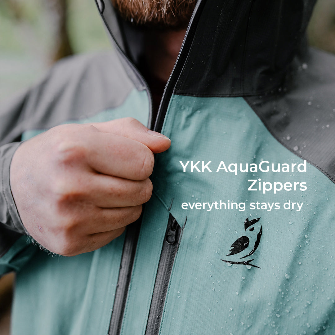 Close-up of a person wearing a waterproof jacket, pulling the zipper with a hand. Water droplets are visible on the jacket, and white text reads 'YKK AquaGuard Zippers everything stays dry'.