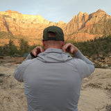 rear view of man pulling up hood of gray sun shirt near desert mountain