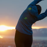 woman wearing technical hoodie while stretching after trail run back view