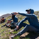 Backpackers wearing the Altitude Sun Hoodie resting on a mountain ridge under bright blue skies.