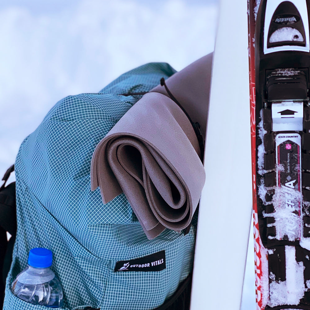 closed cell foam pad rolled up on top of backpack leaning on skiis