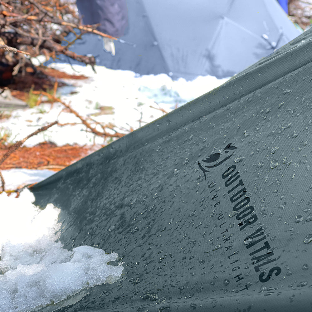 close view of the edge of a trekking pole tent partially covered in snow