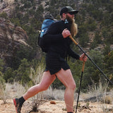 Hiker in the Altitude Sun Hoodie trekking through desert terrain with trekking poles and backpack.