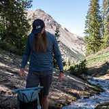 Hiker wearing the Altitude Sun Hoodie with Shadowlight Backpack with mountains and trees in the background.