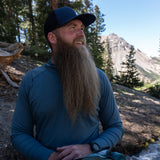 Hiker wearing the Altitude Sun Hoodie with mountains and trees in the background.