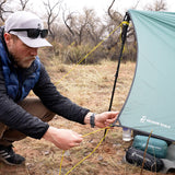 side view of man adjusting corner of tarp shelter pitched on ground