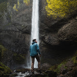 rear view of man wearing blue Ventus Hoodie in front of waterfall near cliff