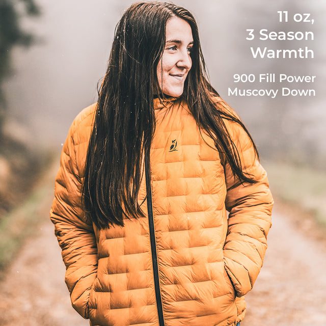 A person wearing a quilted mustard-yellow puffer jacket outdoors, with text overlay on the right reading '11 oz, 3 Season Warmth, 900 Fill Power Muscovy Down'.
