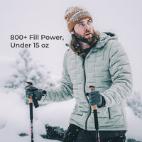 A man in a snowy outdoor setting wearing a light gray puffer jacket, a brown knit beanie, and ski gloves, holding ski poles. Text on the left reads '800+ Fill Power, Under 15 oz'.