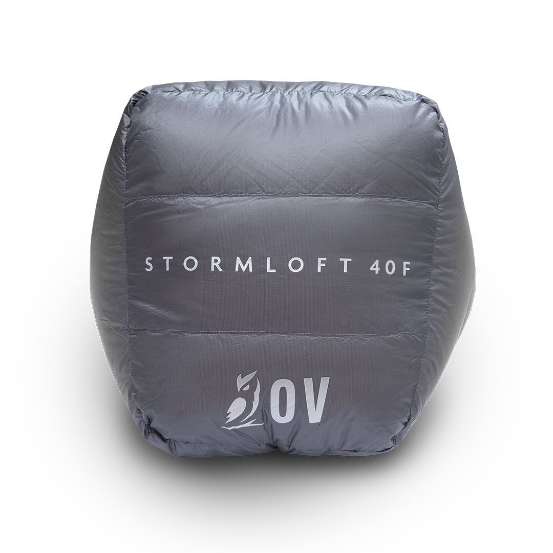 Bottom view of the black Outdoor Vitals StormLoft 40F topquilt packed inside its compression stuff sack, displaying the printed product name and OV owl logo.