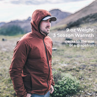 A man wearing a hooded lightweight jacket stands outdoors in a grassy mountain landscape. White text on the right reads '9 oz Weight 3 Season Warmth packs to the size of a grapefruit'.