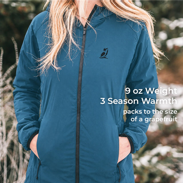 A woman wearing a teal blue lightweight zip-up jacket outdoors, with text overlay on the right reading '9 oz Weight 3 Season Warmth packs to the size of a grapefruit'.