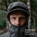 A close-up portrait of a man wearing a waterproof hooded jacket in a blurred outdoor forest setting. The hood is up, covering his face, with the text 'Anatomical Hood turns with you' in the lower right corner.