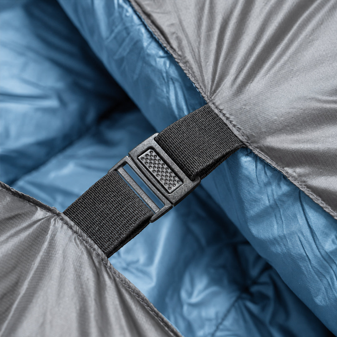 Close-up of a buckle and strap securing two sides of a backpacking quilt with a blue interior together.