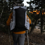 Rear view of hiker wearing Carbon Evo 50 backpack with side water bottle pockets while hiking through forest at dusk